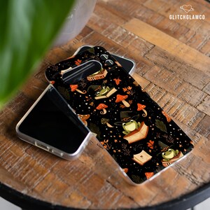 May include: A black phone case with a repeating pattern of green frogs wearing witch hats, sitting on books with mushrooms and stars.