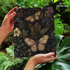 May include: A rectangular art print featuring a dark background with a botanical design. Two large butterflies with cream-colored wings are prominent, surrounded by flowers and foliage in shades of green, purple, and yellow. The print is held by hands.