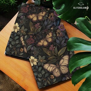 May include: A dark-colored tablet case featuring a botanical design with butterflies and flowers in shades of yellow, brown, and purple. The case is set on a wooden surface, with the GlitchGlamCo logo visible.