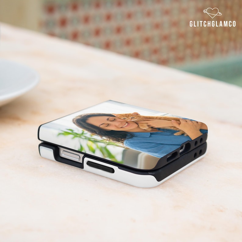 May include: A white and black phone case with a photo of a woman holding a cat. The phone case is folded in half. The text "GLITCHGLAMCO" is in the upper right corner.