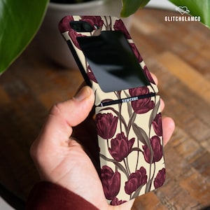 May include: A cream-colored phone case with a floral design featuring dark red tulips. The case is designed for a Samsung foldable phone.