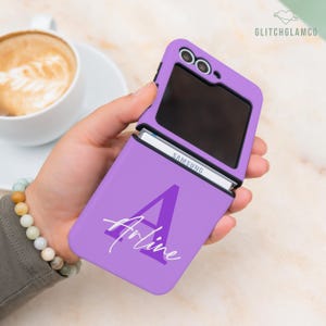 May include: A lavender Samsung phone case with the name "Arline" in white script and a large letter "A". The phone case is open, revealing the phone's screen and the Samsung logo. The case has a camera cutout.