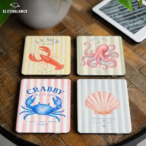 May include: A set of four square coasters featuring nautical illustrations. One shows a red lobster on yellow stripes, one a pink octopus on green stripes, one a blue crab on pink stripes with text CRABBY but cute, and one a seashell on blue stripes.