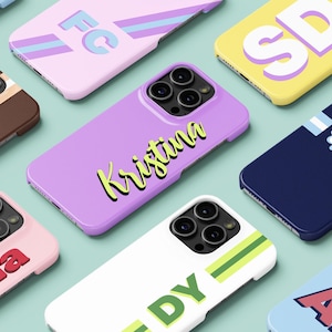 Könnte beinhalten: Eine Sammlung personalisierter Handyhüllen in verschiedenen Farben, darunter Rosa, Lila, Gelb und Blau. Jede Hülle hat ein einzigartiges Design mit Namen oder Initialen in fetten, farbenfrohen Schriftarten. Die Hüllen sind für ein Smartphone konzipiert.