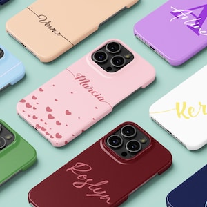 May include: A collection of personalized phone cases in various colors, including pink, green, and navy. Each case features a name in a stylish script font. Some cases have heart patterns or initials.