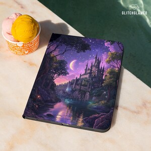 May include: A tablet case with a fantasy castle scene in purple, blue, and green hues. The image includes a river and moon. The case is on a marble surface, next to a cup of ice cream.