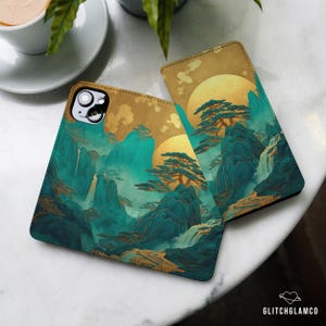 May include: Two rectangular phone cases featuring a landscape illustration of teal mountains, pine trees, and waterfalls set against a large golden sun. The cases have a smooth finish and a cutout for the camera lens on the top left corner.