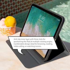 Pu&ograve; includere: Una custodia nera per iPad con uno schermo che mostra una scena di spiaggia. La custodia &egrave; aperta, sostenendo l'iPad. Lo schermo mostra l'ora: 8:46. La custodia ha uno strato interno antiscivolo e pi&ugrave; angolazioni.