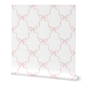Può includere: Un rotolo di carta da parati con un motivo ripetuto di fiocchi rosa chiaro collegati da linee ondulate su sfondo bianco. I fiocchi sono disegnati con un effetto pennellata strutturato, creando un design delicato. La carta da parati è arrotolata.