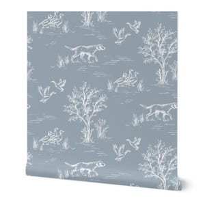 Può includere: Rotolo di carta da parati con un motivo ripetuto di cani, anatre, alberi ed erba bianchi su uno sfondo blu tenue. Il design ha un'estetica classica ispirata alla toile.