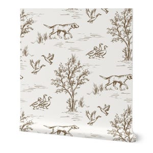 Può includere: Un rotolo di carta da parati con un design toile de Jouy marrone e bianco. Il motivo include illustrazioni di cani, anatre, alberi e aree erbose. Il design è un motivo ripetuto, che crea un'estetica classica e rustica.