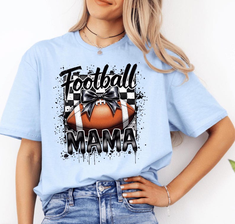 A light blue Football Mama graphic t shirt featuring a stylish football design with a checkered pattern and a bow.