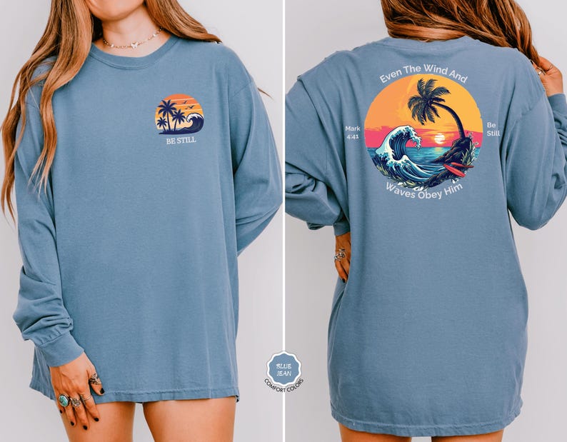 May include: A long-sleeved blue shirt with a front graphic of a sunset, palm trees, and waves, with the text "BE STILL." The back of the shirt features a larger graphic with the text "Even The Wind And Waves Obey Him."