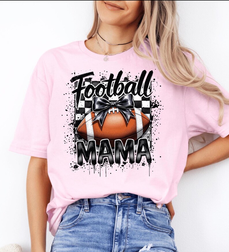 A light pink Football Mama graphic t shirt featuring a stylish football design with a checkered pattern and a bow.