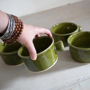 A hand thrown mug with a v shape and a knob handle