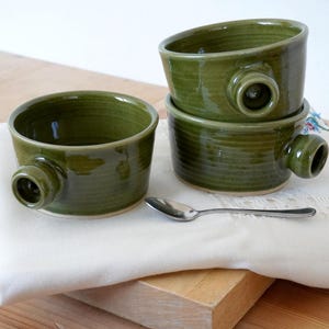 A hand thrown mug with a v shape and a knob handle