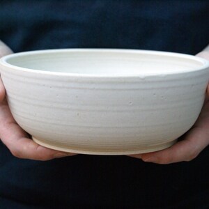 Two hands holding a large salad bowl glazed in matt vanilla cream