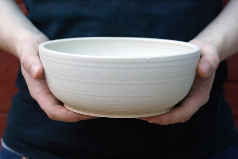 Two hands holding a large salad bowl glazed in matt vanilla cream