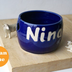 A pottery yarn bowl with the name 'Nina' on the side glazed in glossy ocean blue