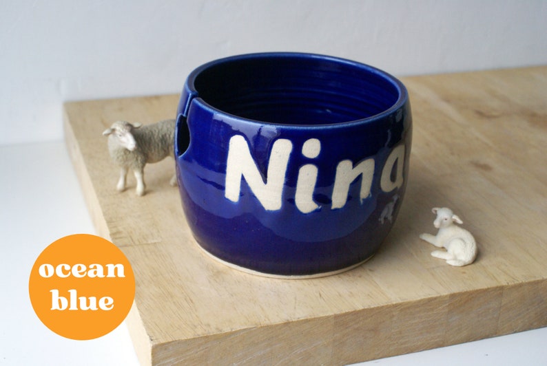 A pottery yarn bowl with the name 'Nina' on the side glazed in glossy ocean blue