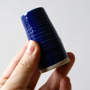 May include: A small, blue ceramic vase with a white rim. The vase has a textured, striped pattern.