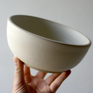 One hand holding a large salad bowl glazed in matt vanilla cream