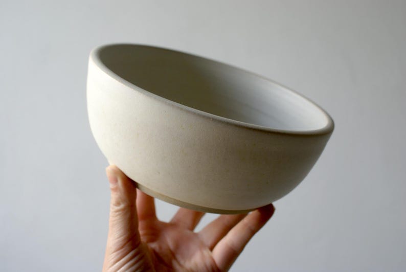 One hand holding a large salad bowl glazed in matt vanilla cream