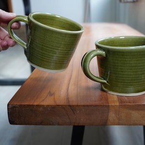 Una taza hecha a mano con una rana en el fondo, esmaltada en verde brillante.