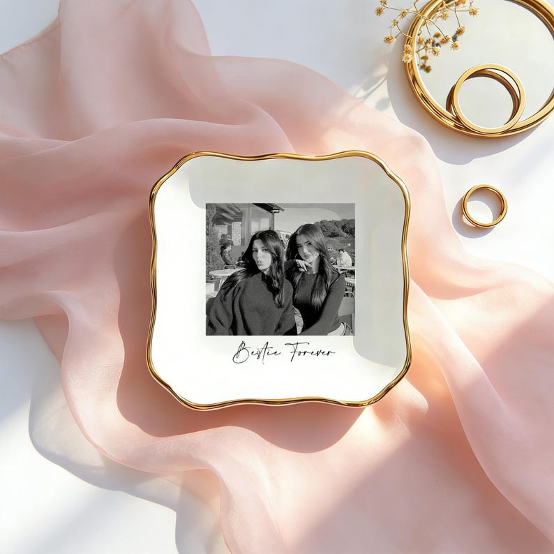 May include: A square white ceramic trinket dish with scalloped edges and a gold-toned rim. The center features a black and white photograph of two people with the cursive text Bestie Forever printed underneath the image on the white surface.