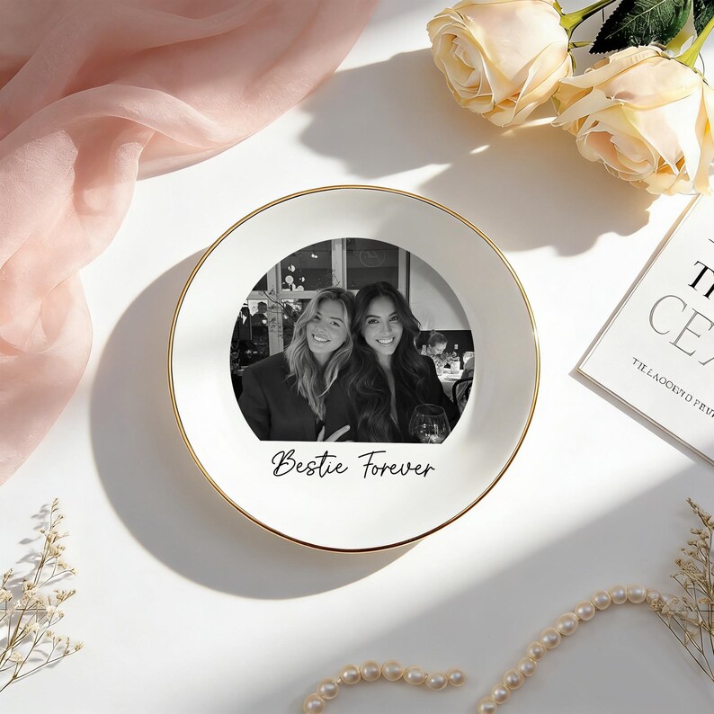 May include: A round white ceramic trinket dish with a gold-trimmed edge. The center features a black and white photograph of two people smiling, with the text "Bestie Forever" printed in a black cursive script directly below the image.
