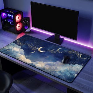 May include: A blue and gold galaxy-themed mouse mat with a design of clouds, stars, and crescent moons. The mouse mat is on a desk with a computer monitor, speakers, and a keyboard.