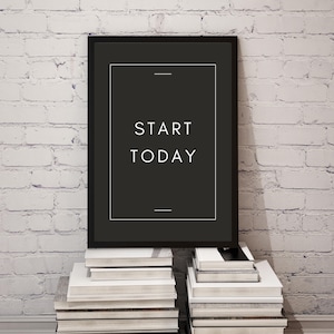 May include: A framed black poster with the words "START TODAY" in white, resting on a stack of books. The poster has a minimalist design with a black background and white text. The background is a white brick wall.