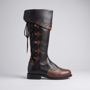 May include: A knee-high boot featuring a dark brown leather upper with a folded cuff at the top. The side of the boot displays a black lace-up closure system with brown leather tabs, a rounded toe, and a low black heel with a textured finish.