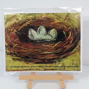 May include: A card with a painting of a bird's nest with eggs. The text on the card reads: "...It always protects, always trusts, always hopes, always perseveres. Love never fails..." I Corinthians 13:7-8
