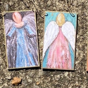 May include: Four painted wooden angel ornaments with gold string hangers. The angels are painted in various colours, including yellow, blue, pink, and white. The angels have wings and are depicted in a variety of poses.