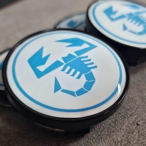 Può includere: Quattro coprimozzi neri e bianchi con un logo di scorpione blu. Lo scorpione è stilizzato e ha un contorno bianco.