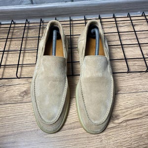 Op de afbeelding: Een paar beige su&egrave;de instaploafers met een ronde neus, zichtbare stiksels langs de wreef en een lichtgekleurde rubberen zool. Elke schoen bevat een zilverkleurige plastic schoenspanner om de vorm van het schoeisel te behouden.