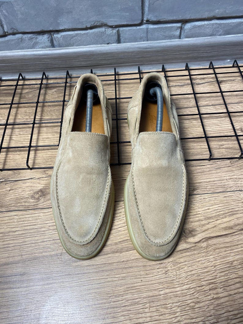 Op de afbeelding: Een paar beige su&egrave;de instaploafers met een ronde neus, zichtbare stiksels langs de wreef en een lichtgekleurde rubberen zool. Elke schoen bevat een zilverkleurige plastic schoenspanner om de vorm van het schoeisel te behouden.