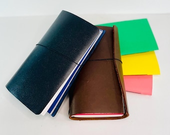 May include: Two leather-bound journals, one dark blue and one brown, with elastic closures. The journals are stacked on top of colorful paper sheets.