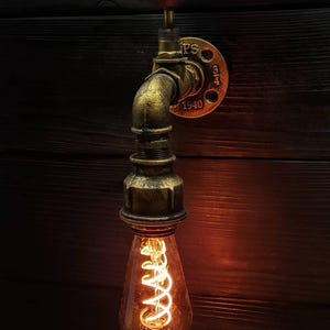 Puede incluir: Una tubería de metal de color dorado con una perilla roja en la parte superior, una bombilla y una placa de metal con el texto "IPS 3/4 1940".