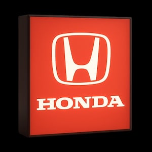 Op de afbeelding: Een vierkant, verlicht bord met het Honda-logo. Het bord heeft een wit Honda-embleem en het woord "HONDA" in witte letters op een rode achtergrond. Het heeft een donkerbruine rand en staat tegen een zwarte achtergrond.