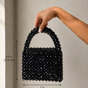 Puede incluir: Un bolso de mano de cuentas negras con cuerpo cuadrado y asa redondeada. El bolso est&aacute; construido con peque&ntilde;as cuentas negras facetadas. Las dimensiones son 21,6 cm de alto y 17,8 cm de ancho, seg&uacute;n lo indicado por los marcadores de medida.