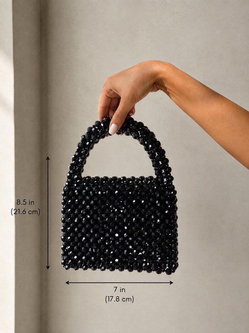 Puede incluir: Un bolso de mano de cuentas negras con cuerpo cuadrado y asa redondeada. El bolso est&aacute; construido con peque&ntilde;as cuentas negras facetadas. Las dimensiones son 21,6 cm de alto y 17,8 cm de ancho, seg&uacute;n lo indicado por los marcadores de medida.