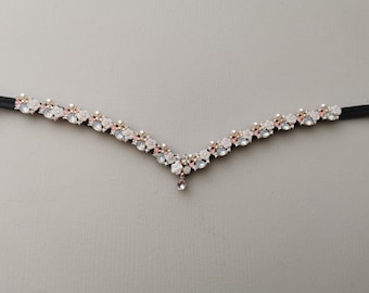 May include: A delicate, V-shaped bridal headpiece with a floral design. The headpiece is adorned with white and pink flowers, rhinestones, and pearls. A single rhinestone dangles from the centre of the piece.