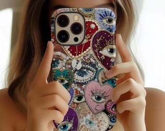 May include: A decorative phone case featuring a collage of heart shapes and eye designs in various colors. The case has a mix of textures, including beads and embroidery, with a dark camera cutout.