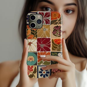 Puede incluir: Una funda de teléfono colorida con un diseño de patchwork que presenta varias flores y formas geométricas. La funda está hecha de plástico duradero y tiene una capa protectora transparente sobre el diseño.