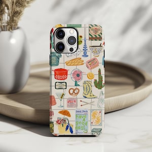 May include: A phone case with a grid pattern featuring various illustrations. The design includes a red pot, a martini glass, a pretzel, a cowboy boot, a cactus, and the text "Have a good day!"