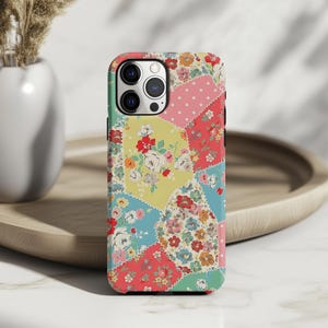 May include: A colorful phone case with a patchwork floral design. The case features a variety of colors, including pink, yellow, blue, and green, with a repeating pattern of floral arrangements. The case is designed to fit a smartphone.