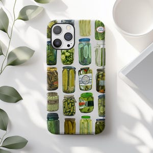 Może przedstawiać: Etui na telefon z wzorem r&oacute;żnych słoik&oacute;w z og&oacute;rkami kiszonymi. Słoiki są wypełnione zielonymi og&oacute;rkami i mają r&oacute;żne etykiety i pokrywki. Tło jest w kolorze jasnoszarym.