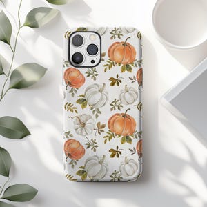 May include: A white phone case featuring a repeating pattern of watercolor pumpkins in shades of orange and white, interspersed with green and brown leaves. The case has a glossy finish and a camera cutout.